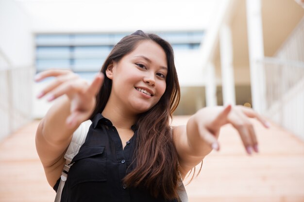 Happy young woman with backpack pointing at camera