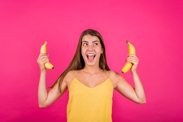 Happy young woman with bananas on pink background