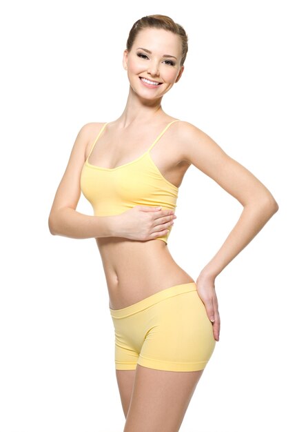 Happy young woman with beautiful slim body in yellow sport clothes -  isolated on white wall