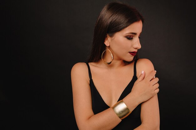 Happy young woman with bright make up and golden jewerly in black dress posing