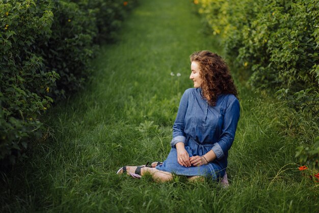 Счастливый молодая женщина с каштановыми вьющимися волосами, носить платье, позирует на открытом воздухе в саду