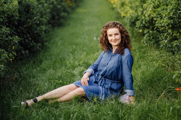 Happy young woman with brown curly hair, wearing a dress, posing outdoors in a garden