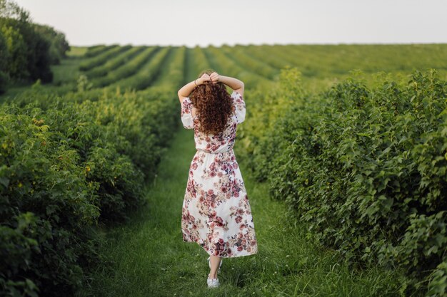 Happy young woman with brown curly hair, wearing a dress, posing outdoors in a garden