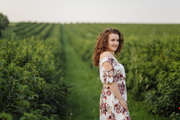 Happy young woman with brown curly hair, wearing a dress, posing outdoors in a garden