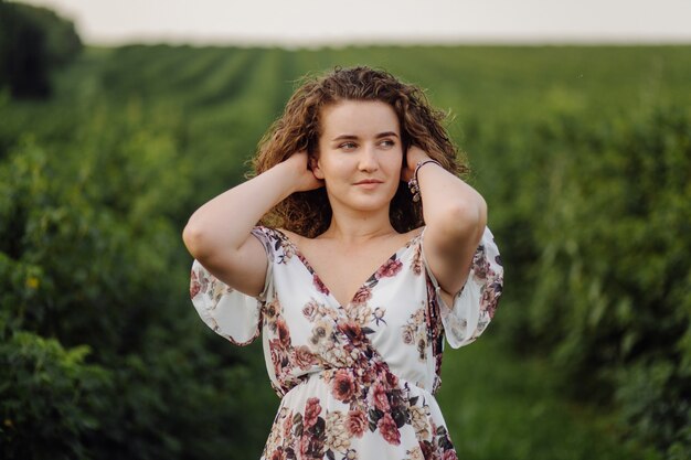 Happy young woman with brown curly hair, wearing a dress, posing outdoors in a garden