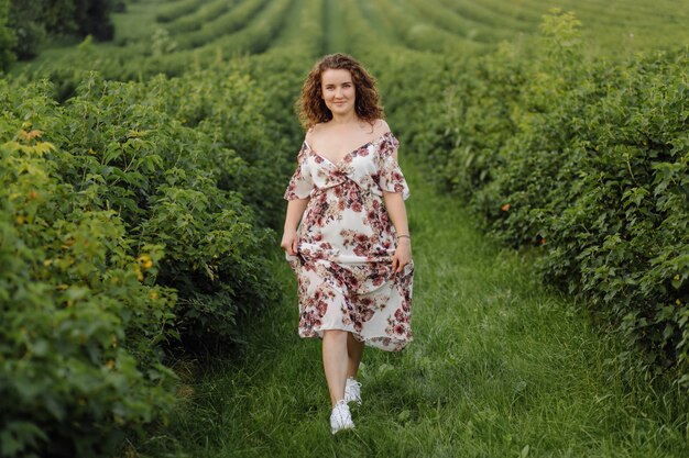 Happy young woman with brown curly hair, wearing a dress, posing outdoors in a garden