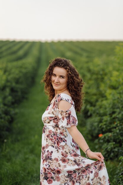 Happy young woman with brown curly hair, wearing a dress, posing outdoors in a garden