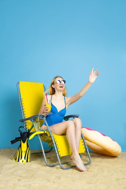 Бесплатное фото Счастливая молодая женщина с коктейлем, улыбаясь, смеясь, приветствуя на синем фоне студии. понятие человеческих эмоций, выражение лица, летние каникулы, выходные. лето, море, океан, алкоголь.