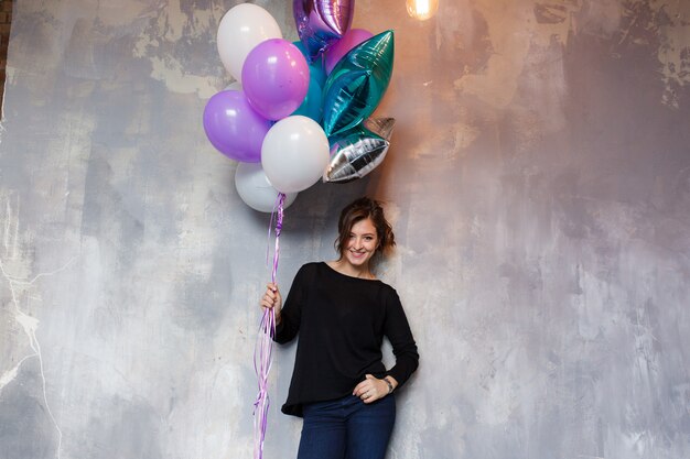 Happy young woman with colorful balloons near an empty gray concrete wall