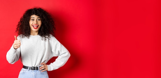 Happy young woman with curly hair praising good work say well done and show thumb up gesture approve