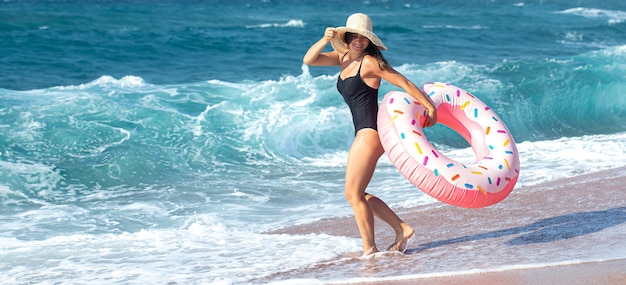 海のそばのドーナツ型の水泳サークルを持つ幸せな若い女性。休暇中のレジャーとエンターテイメントの概念。