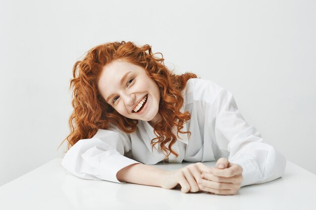 Happy young woman with foxy hair smiling sitting at table.