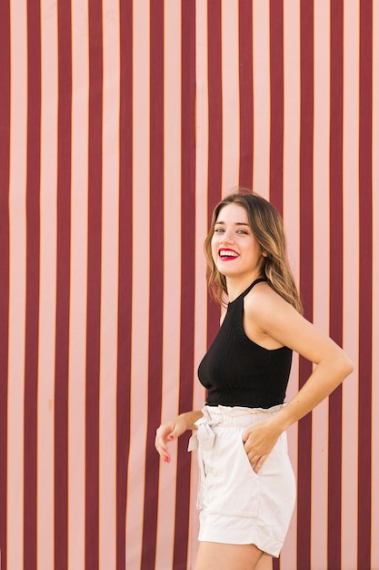 Happy young woman with hand in pocket standing in front of striped background