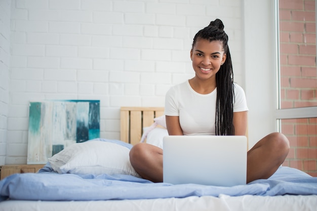 Happy young woman with laptop sitting in bed