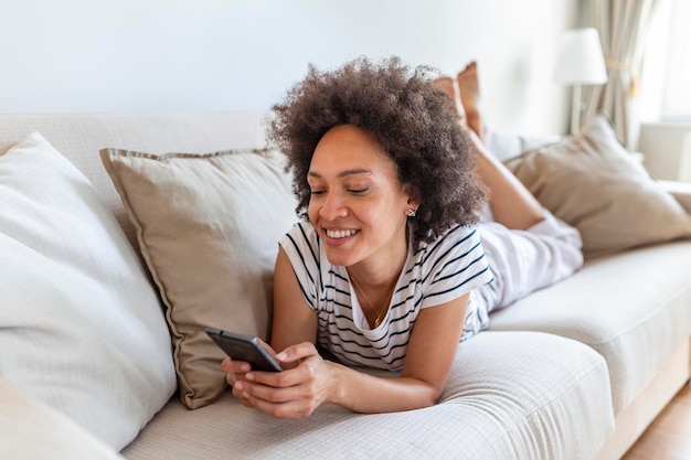 Happy young woman with mobile phone laying on sofa Beautiful young black women using tablet computer