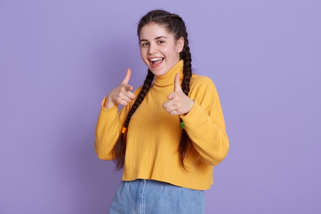 Happy young woman with pigtails pointing with fingers