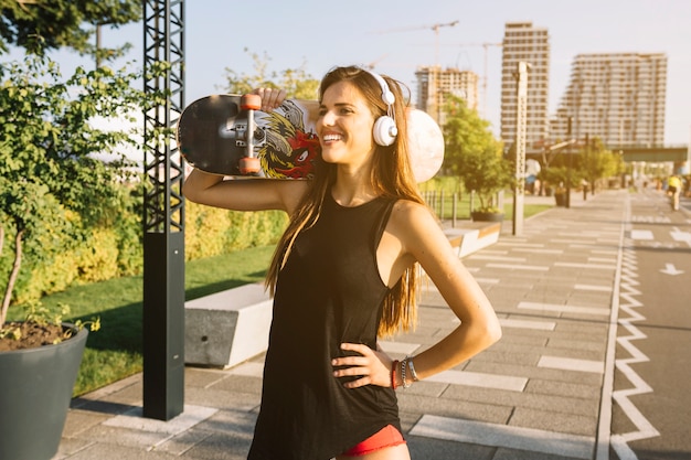 Free photo happy young woman with skateboard standing on sidewalk