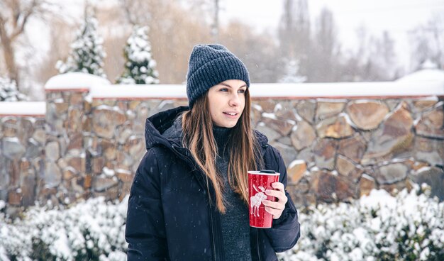 Happy young woman with thermo mug in snowy weather