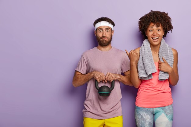 Happy young woman with towel on shoulders points at husband who has surprised expression