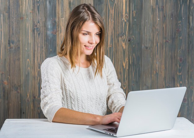 Happy young woman working on laptop against wooden wall