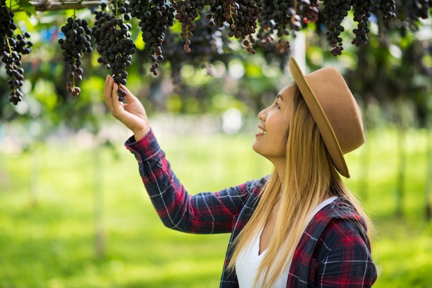 Happy young women gardener holding branches of ripe blue grape