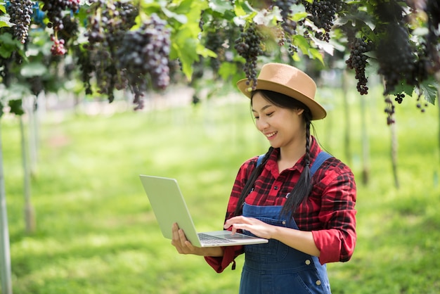 Happy young women gardener holding branches of ripe blue grape