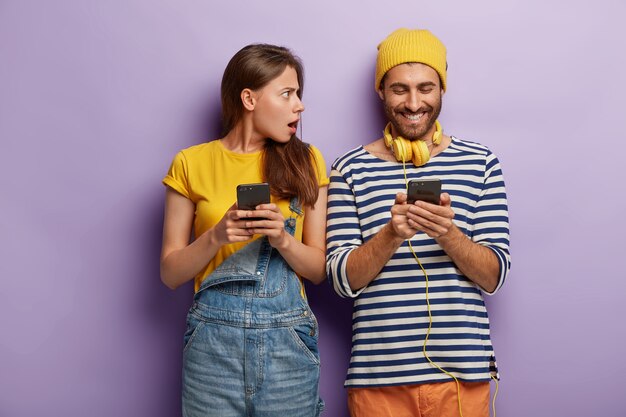 Счастливый мальчик читает посты в социальных сетях, носит наушники, полосатый джемпер, держит современный сотовый телефон, злая женщина