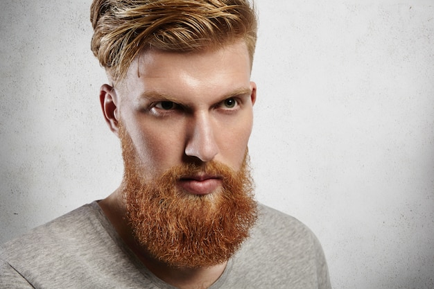 Free photo harsh caucasian man with perfect light skin looking ahead like a brave hero. his fringe is carefully styled and temples are shaved, well-trimmed ginger beard fits him well.
