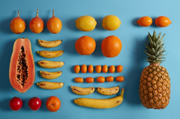 Harvested juicy tropical exotic fruit on blue background. Assortment of papaya, lemons, bananas, pineapple, cumquat, tamarillo. Ingredients for making smoothie. Healthy vegetarian organic food