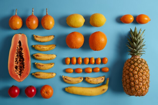 青い背景に収穫されたジューシーな熱帯のエキゾチックなフルーツ。パパイヤ、レモン、バナナ、パイナップル、キンカン、タマリロの品揃え。スムージーを作るための材料。健康的なベジタリアン有機食品