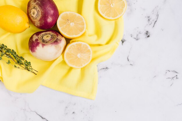 Harvested turnips and halved lemons on yellow tablecloth against white marble backdrop