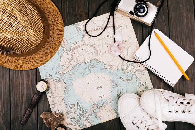 Hat, map, notebook, camera, watch and keds lie on a travel map