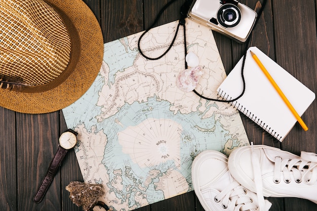 Hat, map, notebook, camera, watch and keds lie on a travel map