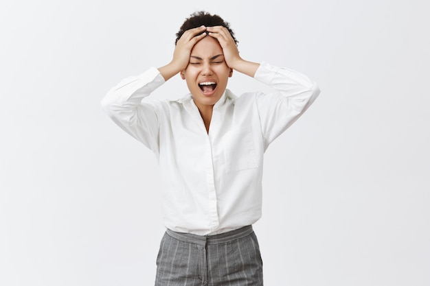 Hate mondays. Unhappy bothered and distressed young determined businesswoman in formal outfit, yelling from stress and unpleasant feelings in soul, holding hands on head, tired and exhausted