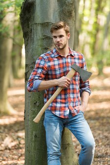 少し休憩します。手に斧を持っている木こり。ワンダーラスト、ハイキング、旅行。斧付きツリーカッター。野生の自然の概念で生き残る。森の中で斧を持つ男。木を切るカッター。 Premium写真