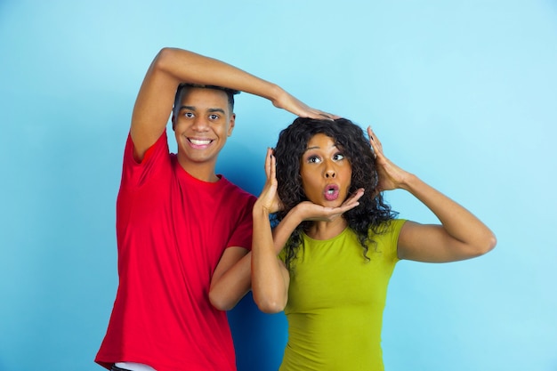 Divertirsi e divertirsi. giovane uomo afro-americano emotivo e donna in abiti casual in posa su sfondo blu. bella coppia. concetto di emozioni umane, espansione facciale, relazioni, annuncio.