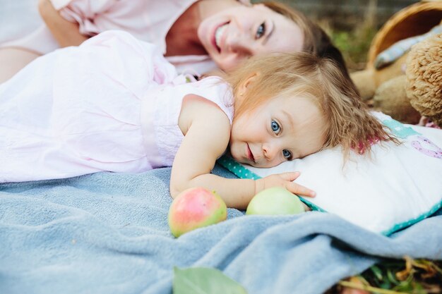 Having fun. Pretty young mother and her little daughter lying on cover in park and having picnic.