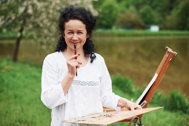 Having fun during the process. Portrait of mature painter with black curly hair in the park outdoors