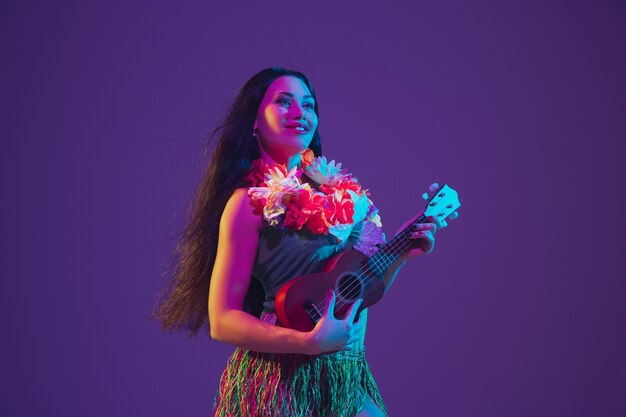 ネオンの光の中で紫の壁に立つハワイの女性ダンサー。