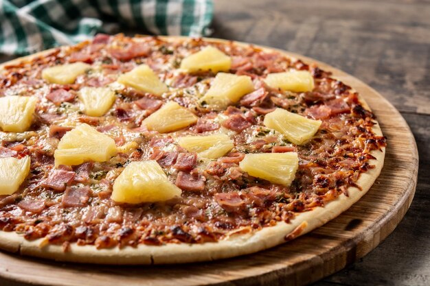 木のテーブルにパイナップル、ハム、チーズをのせたハワイアンピザ