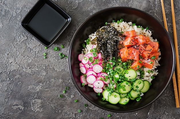 Hawaiian salmon fish poke bowl with rice, radish,cucumber, tomato, sesame seeds and seaweeds. Buddha bowl. Diet food. Top view. Flat lay