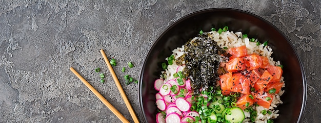 Hawaiian salmon fish poke bowl with rice, radish,cucumber, tomato, sesame seeds and seaweeds. Buddha bowl. Diet food. Top view. Flat lay.