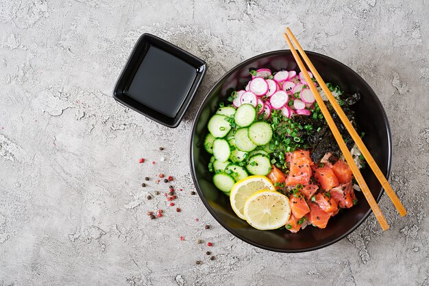 Hawaiian salmon fish poke bowl with rice, radish,cucumber, tomato, sesame seeds and seaweeds. Buddha bowl. Diet food. Top view. Flat lay