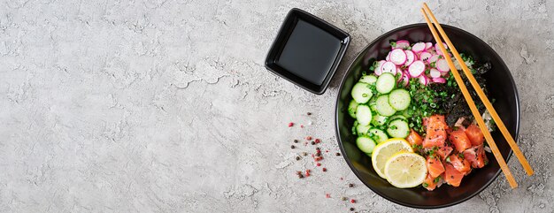 Hawaiian salmon fish poke bowl with rice, radish, cucumber, tomato, sesame seeds and seaweeds. Buddha bowl. Diet food. Top view. Flat lay.