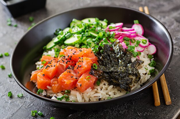 Hawaiian salmon fish poke bowl with rice, radish,cucumber, tomato, sesame seeds and seaweeds. Buddha bowl. Diet food