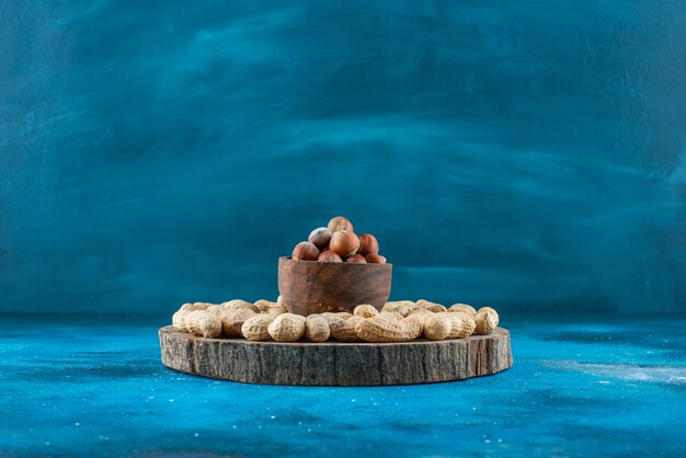 Free photo hazelnuts in a bowl on board with peanuts on the blue surface