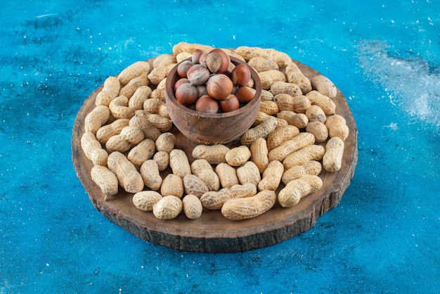 Hazelnuts in a bowl on board with peanuts , on the blue table. 