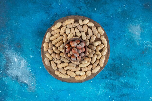 青いテーブルの上に、ピーナッツと一緒にボウルに入れられたヘーゼルナッツ。