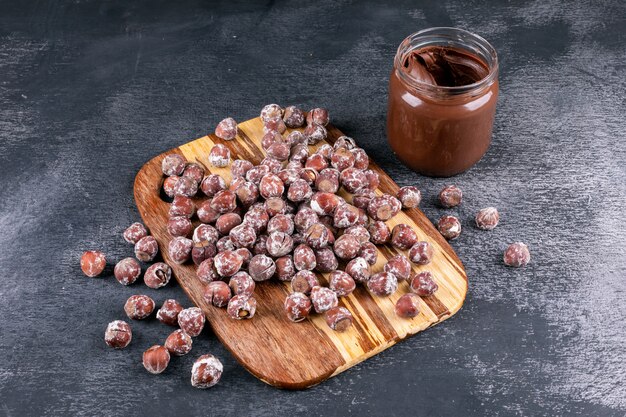Hazelnuts with cocoa spread high angle view on a wooden cutting board and dark stone table