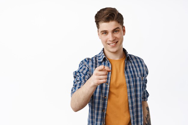 He choose you. Smiling young man, student boy pointing finger at camera, recruiting people, invite for event, join our company gesture, stands against white background